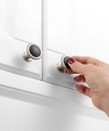 Hand reaching for round cabinet knobs 10 pack matte black and nickel, durable solid metal drawer knobs on white cabinet.