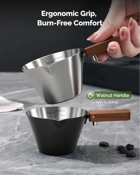 Hand holding Stainless Steel Espresso Measuring Cup With Wide Mouth And V Shaped Pour Spout, easy grip walnut handle visible
