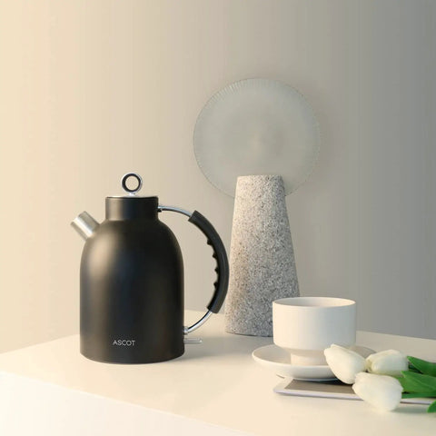 Retro Glass Electric Kettle 1.5 Liters Tea Boiler With Bpa Safe Cordless Setup Straight Up Plastic Free Build And Auto Shut Off Protection In Sleek Black next to a white teacup and flowers.