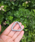 Hand holding Beefy Stainless Steel 316 Marine Grade Triangle Ring Buckle Welded V Shaped Heavy Duty Ring against greenery