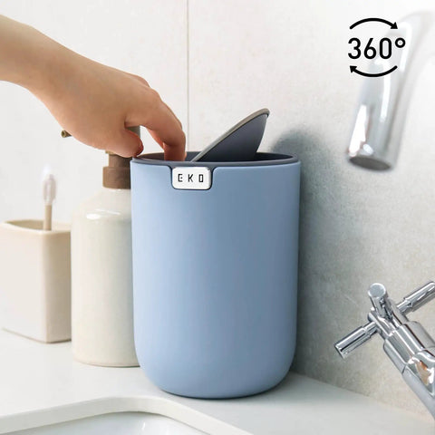 Person placing item in Ultra Compact 1.5L Mini Tabletop Trash Can With Swing Lid For Bathroom Vanity Or Desk Space Saving 4.7 Inch Diameter 6.5 Inch Tall Small Garbage Bin For Office Countertop on sink