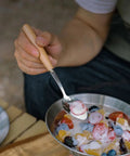 Person using Trail Ready Stainless Steel Camping Utensil Kit spoon to eat fruit salad outdoors