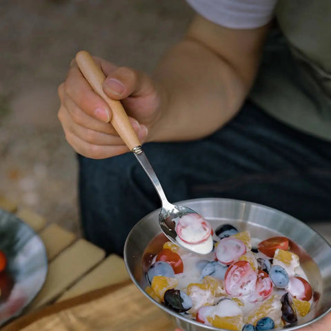 Person using Trail Ready Stainless Steel Camping Utensil Kit spoon to eat fruit salad outdoors