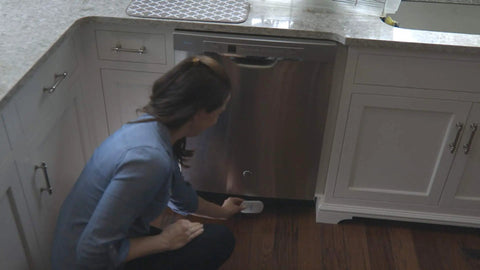 Smart WiFi Water And Freeze Detector With 80dB Audible Alarm Text And Email Alerts placed under a dishwasher by a person