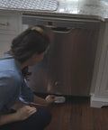 Woman setting up Smart Water Leak And Freeze Detector With WiFi Alerts, 80dB Audible Alarm under a kitchen dishwasher