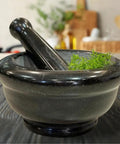Heavy Duty Granite Mortar And Pestle Set 6 Inch Stone Grinder For Fresh Guacamole Salsa And Pesto Crush Herbs And Spices With Ease Non Slip Base Durable Black Kitchen Essential with herbs visible inside.