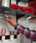 Person applying Ultra Tough Industrial Hook And Loop Fasteners With Stick-On Adhesive For Indoor Outdoor Use One And Seven Eighths Inch Circular Pads under shelf in garage