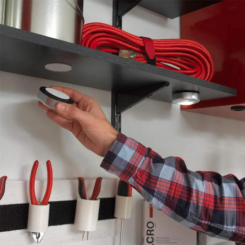 Person applying Ultra Tough Industrial Hook And Loop Fasteners With Stick-On Adhesive For Indoor Outdoor Use One And Seven Eighths Inch Circular Pads under shelf in garage