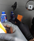 Two blue CARPRO CQUARTZ UK 3.0 ceramic coating bottles with orange applicator pad and gloved hands