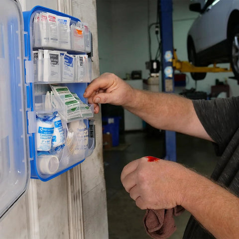 Blue wall-mounted first aid kit with clear pockets containing bandages and supplies; person selecting an item