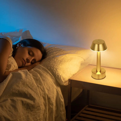 Cordless Gold Battery Operated Table Lamp For Dining Ambience on bedside, emitting warm light, enhancing room decor.