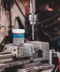 Close-up of a drill press with Boss Grade Synthetic Lubricant Paste For MQL Metalworking Industrial Pink Hard Paste Multi Use 4 Oz jar nearby.