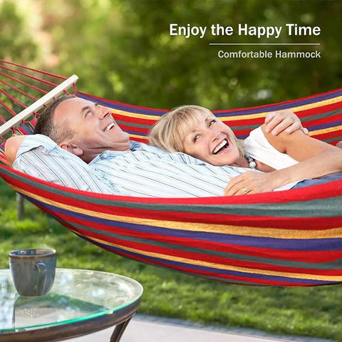 Two people relaxing in a Heavy Duty Canvas Camping Hammock With Thick 320G Fabric, 550Lb Load, Anti Roll Balance Beams, in a garden.