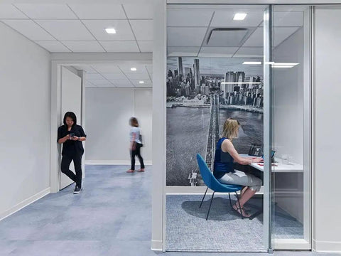 Modern office with glass wall, woman working in a cubicle, white walls equipped with White Vinyl Wall Base Self-Stick Ultra Thick 1/8 Inch, 4.25 Inch By 80 Feet Peel And Stick Adhesive Backing, Flexible Floor Base Trim For Walls And Baseboards, Toe-Friendly Easy Install, Durable, Easy To Clean