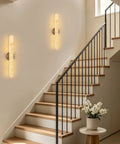 Natural Alabaster Brass Wall Sconce glowing on wall beside modern staircase with wooden steps, 24 inches tall.