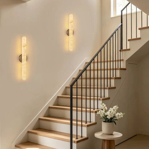 Natural Alabaster Brass Wall Sconce glowing on wall beside modern staircase with wooden steps, 24 inches tall.