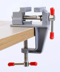 3.5 Inch Compact Aluminum Swivel Mini Bench Vise with red handles, clamped on a table edge for Jewelry Making Hobby Craft Model Building and Electronics Repair On The Go Ready Ultra Portable Durable Rust Resistant Clamp Tool.