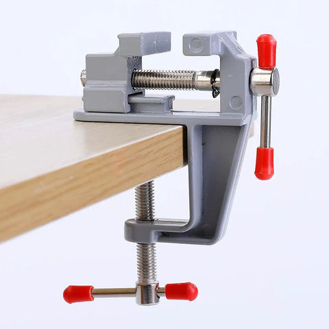 3.5 Inch Compact Aluminum Swivel Mini Bench Vise with red handles, clamped on a table edge for Jewelry Making Hobby Craft Model Building and Electronics Repair On The Go Ready Ultra Portable Durable Rust Resistant Clamp Tool.