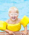 Happy child wearing Heavy Hitting Splash Guard Safety Glasses Six Pack with yellow floatation device by poolside.