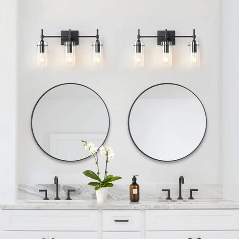 Three Light Black Vanity Light Fixture Over Mirror With Clear Glass Shades For Sleek Modern Bathroom E26 Bulb Compatible Industrial Farmhouse Style Wall Lighting mounted above dual mirrors on white wall.