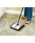 Lightweight Manual Carpet And Hard Floor Sweeper Featuring Dual Rotating Brush Roll Plus Corner Edge Brushes picking up cereal from tile floor.