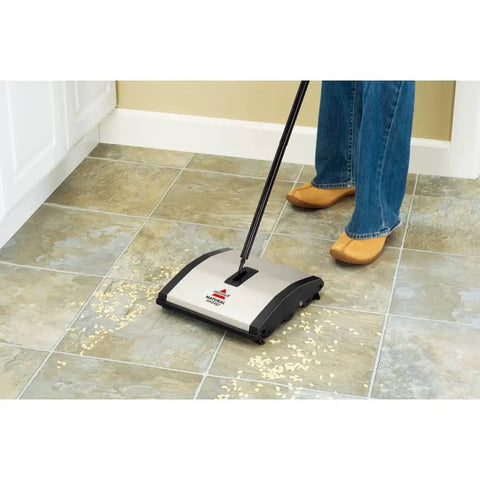 Lightweight Manual Carpet And Hard Floor Sweeper Featuring Dual Rotating Brush Roll Plus Corner Edge Brushes picking up cereal from tile floor.