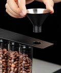 Glass Coffee Bean Storage Tubes Set Of Six With One Way Degassing Valve And Magnetic Stand And Single Dose Espresso Dosing Vials being filled with coffee using a funnel.