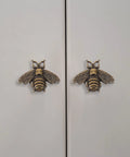 Close-up of two vintage gold bee shaped cabinet knobs on white cabinet doors, part of a set of 10 vintage gold bee shaped cabinet knobs made from zinc alloy hardware for cabinets and dressers retro bronze finish drawer knobs pull handles for dresser drawers durable rust resistant and stylish cabinet hardware.