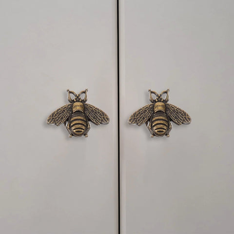 Close-up of two vintage gold bee shaped cabinet knobs on white cabinet doors, part of a set of 10 vintage gold bee shaped cabinet knobs made from zinc alloy hardware for cabinets and dressers retro bronze finish drawer knobs pull handles for dresser drawers durable rust resistant and stylish cabinet hardware.