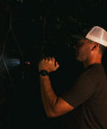 Person using Beefed Up 2000 Lumen Rechargeable Flashlight For Outdoor Adventures, illuminating a dark forest area at night.
