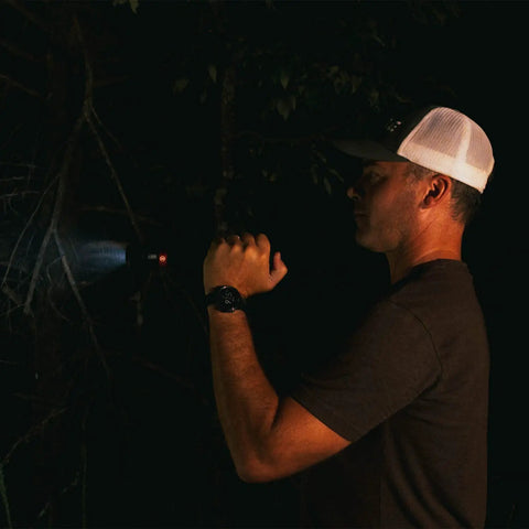 Person using Beefed Up 2000 Lumen Rechargeable Flashlight For Outdoor Adventures, illuminating a dark forest area at night.