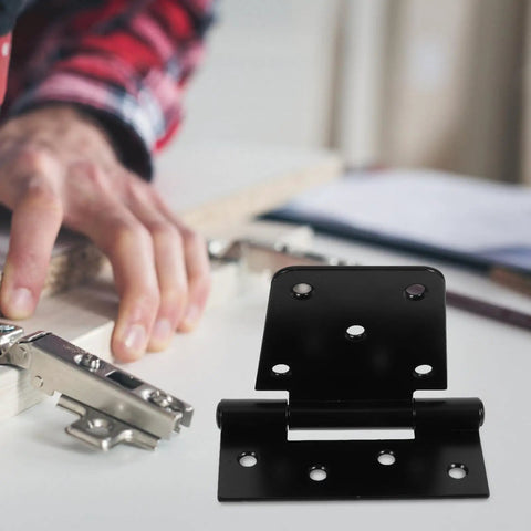 Heavy Duty Furniture Hinges Set In Black Carbon Steel With Screws, shown on a table with a person assembling furniture nearby.