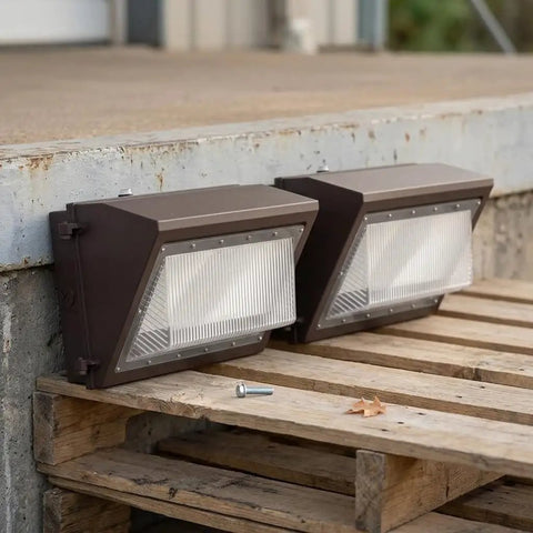 CONGARTENO Outdoor Security Flood Light 2 Pack Dusk to Photocell Wall Mount placed on a wooden pallet with a screw nearby.