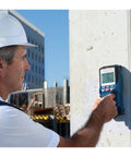Tough As Nails Stud Finder Wall Scanner With Dead On Digital Display in use on a concrete wall by a worker wearing a hard hat.