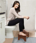 Woman using Wooden Toilet Stool For Kids And Adults, Anti Slip Bamboo Potty Training Step Stool, 7 Inch Rise, in bathroom setup.