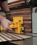 Person using GRR RIPPER GR 100 3D Adjustable Table Saw Pushblock 2 Pack Delivers Pro Grade Precision And Kickback Control With A Rock Solid Grip Keeping Your Hands Safe While You Push Through Lumber For Smooth Accurate Cuts Every Time In Bright Yellow on striped wooden board