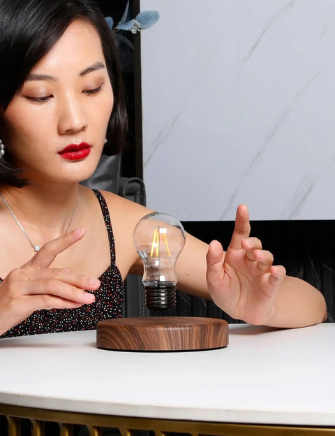 Person interacting with Levitating Bulb Lamp With Magnetic Floating Light For Home Office And Desk Decor A Totally Cool Tech Gadget Gift For Him And Her Perfect Valentine Gift For Him And Her Or Christmas Birthday Present, featuring a floating light bulb above a wooden base on a desk.