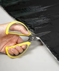 Hand using scissors to cut Top Shelf Self Adhesive Roofing Felt Repair Tape Built Badass To Stop Leaks And Seal Surface Cracks Fast.