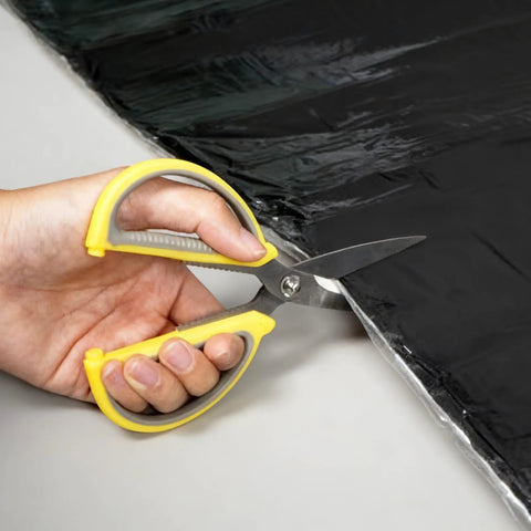 Hand using scissors to cut Top Shelf Self Adhesive Roofing Felt Repair Tape Built Badass To Stop Leaks And Seal Surface Cracks Fast.