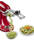7 Blade Spiralizer Plus with Peel Core and Slice Attachment for stand mixer in red, spiralizing cucumber into a bowl.