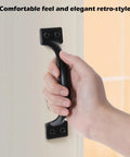Hand grasping black iron handle from Six-Piece 5 Inch Rustic Gate Handle Set - Built Tough Heavy-Duty Iron Door Pulls With Screws For Barn Doors.