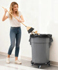 Person using broom next to trash can on adjustable 15-19 inch round drum dolly with locking wheels, heavy duty 440 lbs cart stand