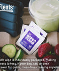 Close-up of individually wrapped pre-moistened lens wipes for glasses and shades next to fruit, ideal for travel use.