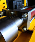 Side view of stainless steel waterjet intensifier pump assembly with mounting bolts on yellow machinery.