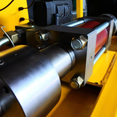 Side view of stainless steel waterjet intensifier pump assembly with mounting bolts on yellow machinery.
