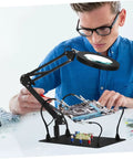 Adjustable Soldering Workbench Clips Set With Iron Alligator Clamps For Electronics Repair Totally Handy Third Hand Fixture Lamp Clamps And Magnifying Glasses For Precision DIY Projects in use by a person working on a circuit board.