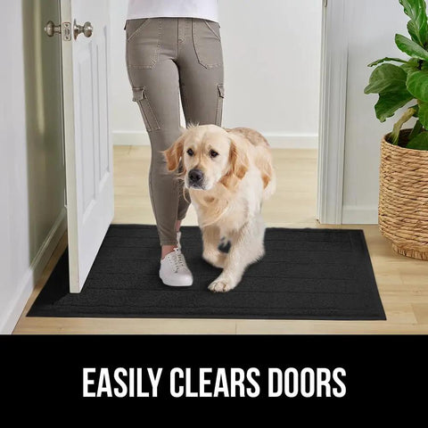 Mesh Weave Dirt Grabbing Doormat For Indoor Outdoor Use With Low Profile Entry Mat 35x23 Heavy Duty Black Welcome Mat That Captures Mud Dirt And Messes In High Traffic Areas in front of an open door with a person and a dog.