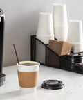 12 Oz Disposable Coffee Cups With Lids And Heat Resistant Sleeves, 100 Sets For Grab And Go Coffee next to coffee maker