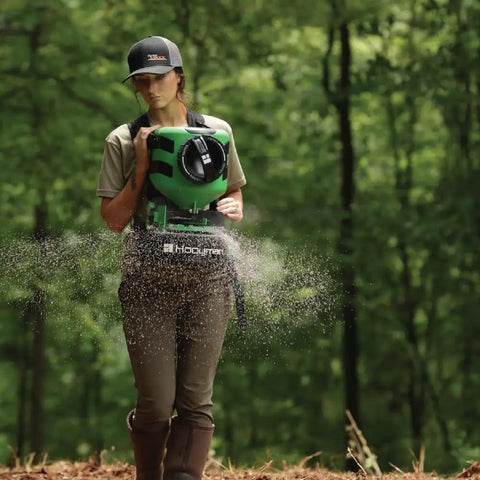 Person using Manual Seed Spreader With 35 Pound Hopper For Food Plots And Land Management Detachable Harness 10 To 20 Foot Throw Radius