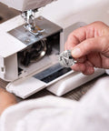 Close-up of a stainless steel sewing machine bobbin case for front-loading machines, held in hand.